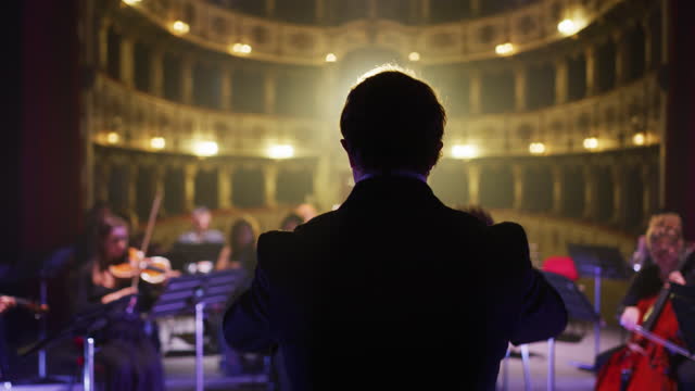 Cinematic shot of conductor directing symphony orchestra with performers playing violins, cello and trumpet
