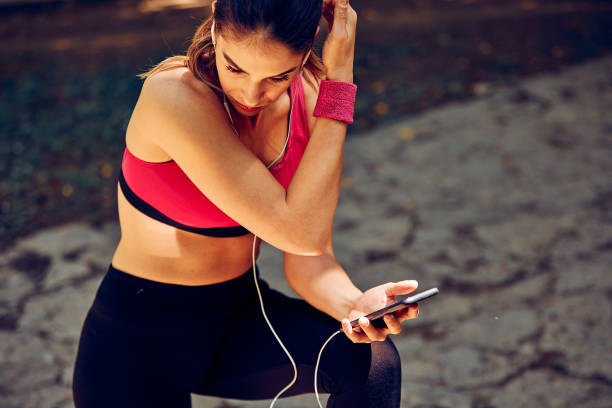 istock Smiling sportswoman crouching, taking a break, and using phone after running in nature. 1288913923