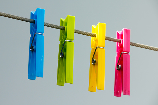 Four colorful clothespins (yellow, green, blue and pink) hanging on the clothesline.