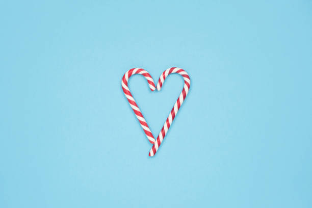 cuore fatto di bastoncini di caramelle su sfondo blu. concetto d'amore minimale. spazio per il testo - peppermint candy stick striped foto e immagini stock