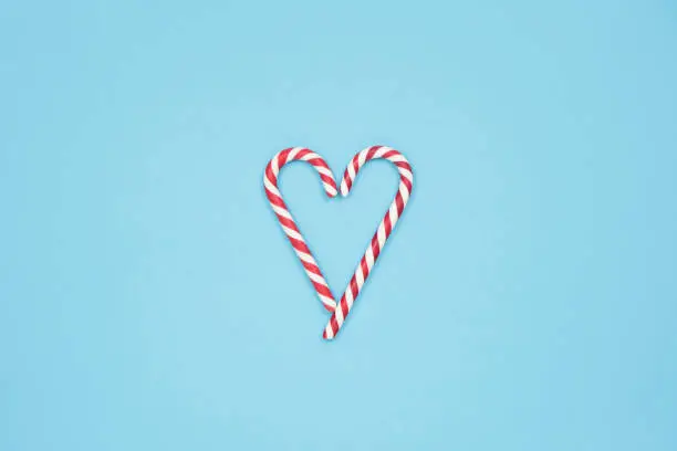 Heart made of candy canes on blue background. Minimal love concept. Space for text