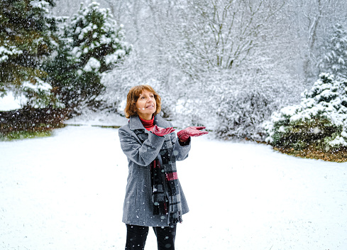 Smiling senior woman standing outdoors enjoying snowfall