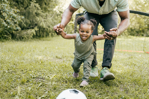 dad helping daughter to kick the soccer ball