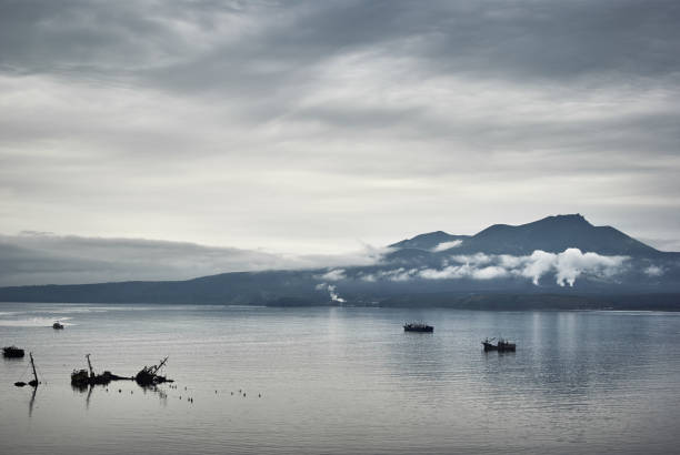 Evening view on volcano of Mendeleev in light fog and ships, dark gloomy sky Evening view on volcano of Mendeleev in light fog and ships, dark gloomy sky. Kunashir island, Kuril islands kunashir island stock pictures, royalty-free photos & images