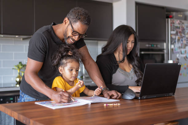 istock Father helping daughter with school assignment while wife works on laptop computer 1288920969