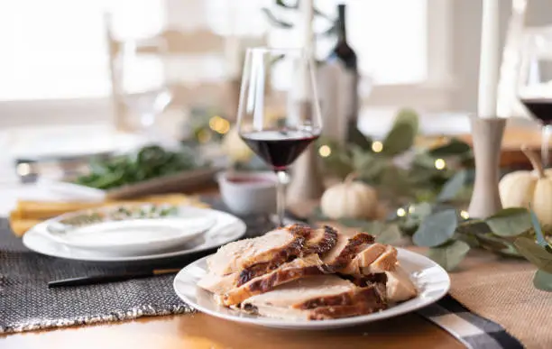 Platter of sliced turkey on a holiday dining table with red wine in blurred background