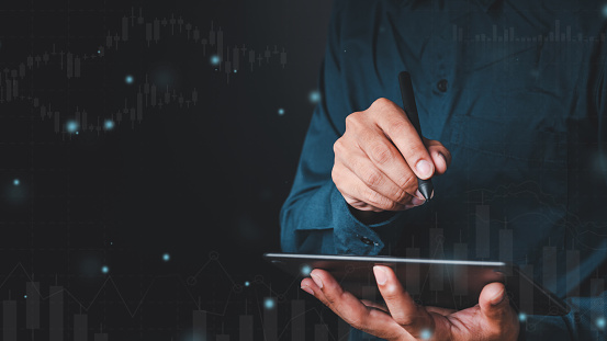 A man is working with a laptop. The other hand holds the globe, graphics, and stock chart. Investment ideas, business concepts, technology concepts.