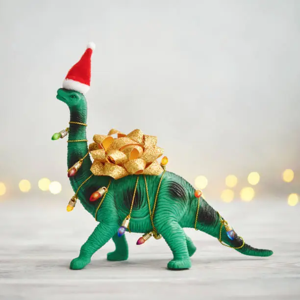 Photo of Christmas Background with Dinosaur Wrapped in Christmas Lights and Bow