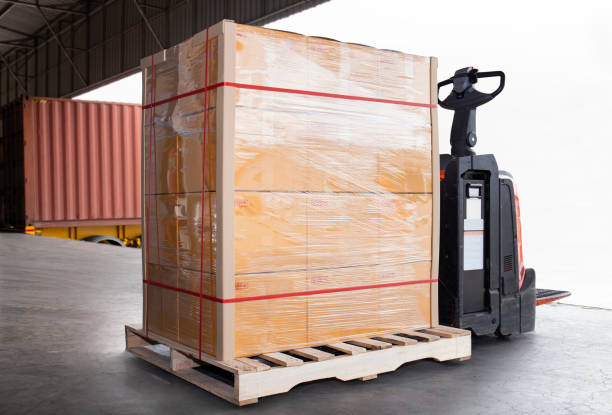 istock Stacked of package boxes on pallet rack and forklift pallet jack waiting to load into shipping container. Cargo shipment boxes, Road freight truck, Warehousing. Logistics and transportation. 1288938609