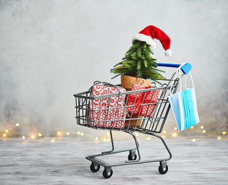 Christmas Shopping and COVID-19. Shopping Cart with Protective Face Mask and Gifts