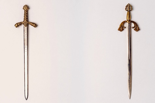 Two ancient knightly swords with golden hilts with engraving isolated on a white background.