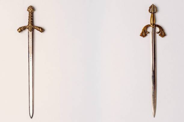 Two ancient knightly swords with golden hilts with engraving isolated on a white background. Two ancient knightly swords with golden hilts with engraving isolated on a white background. Horizontal position, copy space knife weapon photos stock pictures, royalty-free photos & images