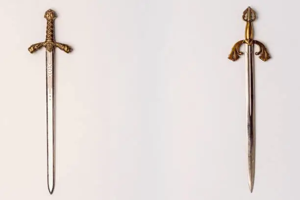 Two ancient knightly swords with golden hilts with engraving isolated on a white background. Horizontal position, copy space