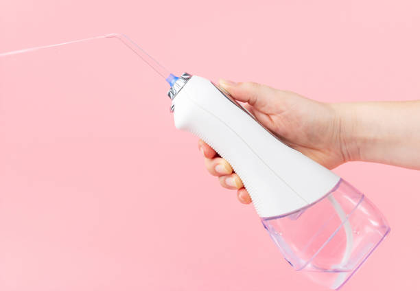 Female hand holds dental irrigator on pink background, copy space