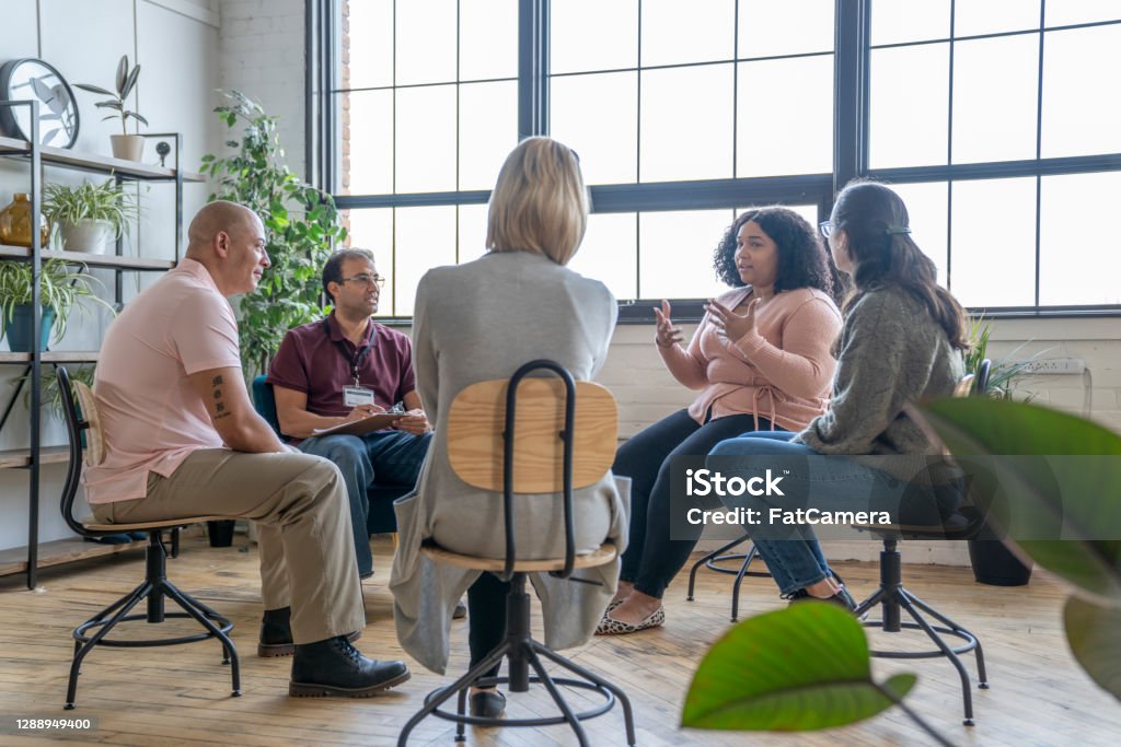Group Therapy Session Multiethnic group of adults gather to discuss their mental health, addictions, and struggles in a group setting with a professional leading the discussion. Addiction Stock Photo