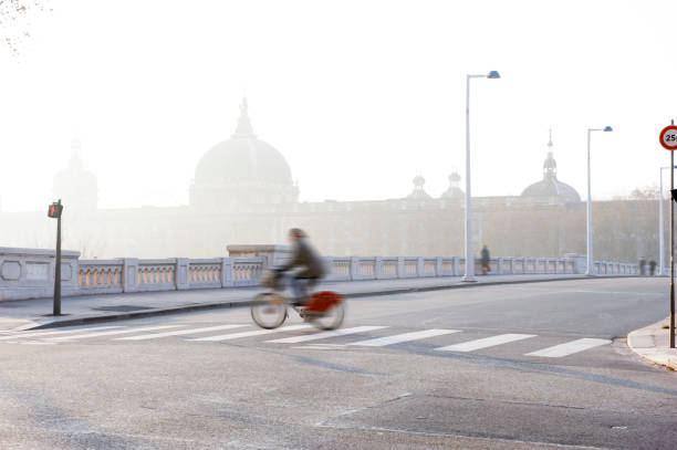 uma mulher de bicicleta atravessa uma rua em uma cidade nebulosa - smog city pollution town - fotografias e filmes do acervo
