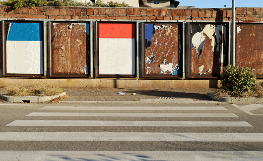 Grunge brick wall covered with street billboards. Some of them blanks,other ripped on a rusty metal plates. Sidewalk and street with crosswalk in front. Background for copy space
