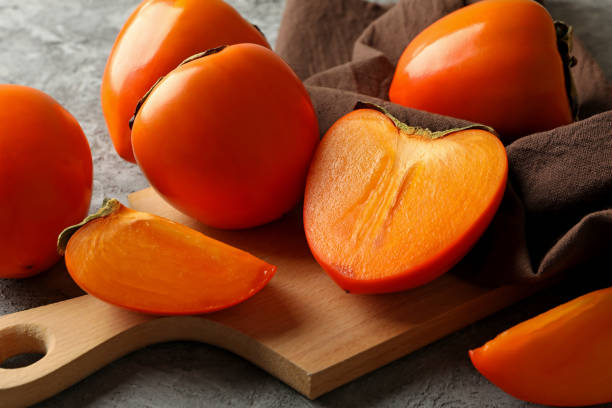 istock Board with ripe persimmon and kitchen towel on gray background 1288961820