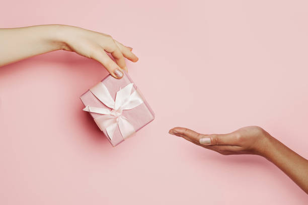 istock Woman hand giving pink gift taking hand on pink, minimal background composition 1288961882