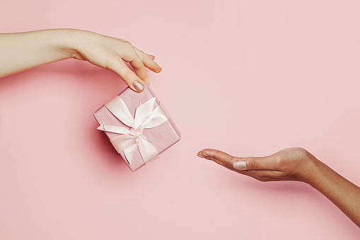 Woman hand giving pink gift taking hand on pink, minimal background composition