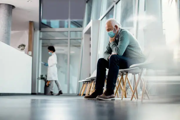 Distraught senior man wearing face mask while sitting alone in hallway at he hospital. Copy space.