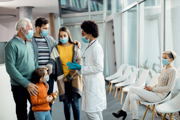 African American doctor talking to extended family at medical clinic during coronavirus pandemic. Extended family and their doctor wearing protective face masks while communicating in a hallway at medical clinic. general practitioner photos stock pictures, royalty-free photos & images