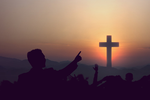 Silhouette of people looking at Christian cross with a sunrise sky background