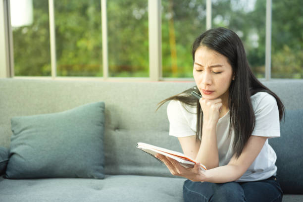 istock Young business asian woman distracted from work and thinking about something on sofa with notebook 1288962993