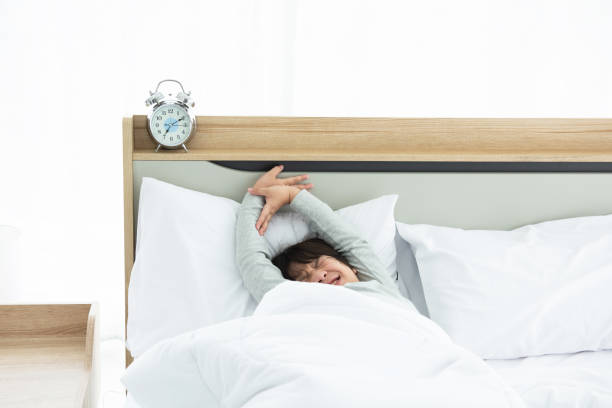 istock boy wakes up and stretching on bed in morning with alarm clock. 1288963341