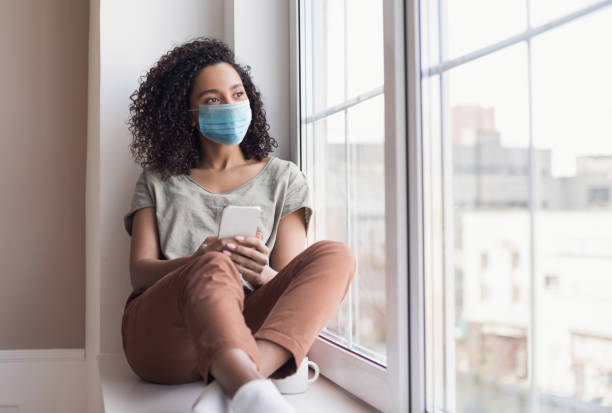 Woman wearing face mask looking at window. Lockdown, social distancing concept