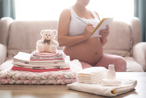 Pregnant woman is getting ready for the maternity hospital, packing baby stuff. pregnant woman preparing and planning baby clothes. Preparing stuff for maternity hospital at home. List of things in the hospital.