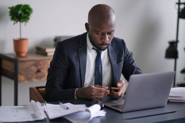 istock Young African executive uses a smartphone, reads bad news and working on a laptop while sitting at his desk in an office. soft focus 1288975164