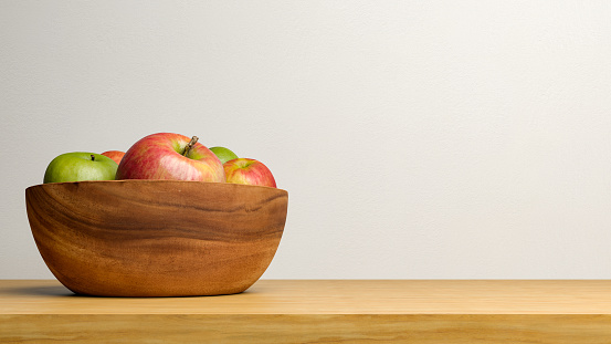 Red and green apples in a bowl, on a wooden table, with empty copy space.