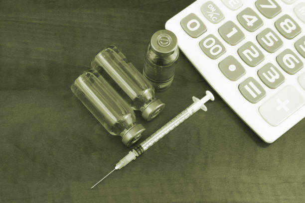 istock Calculator, vaccine and syringe on wooden background. 1288976099