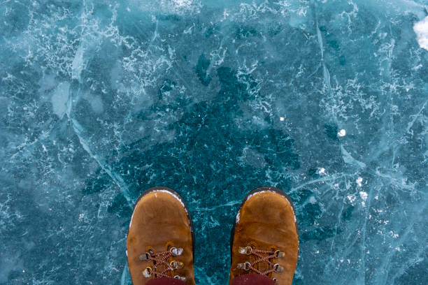 istock Human in brown nubuck boots is standing on cracked blue ice. 1288976434