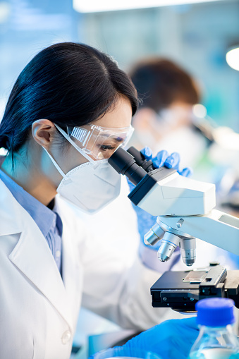 Successful female asian scientist use microscope to check the experiments in the laboratory