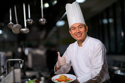 Asian Male chef presenting the dish in the kitchen. Selective focus.