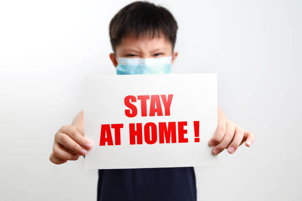 istock Cute boy holding a paper card with text Stay At Home! 1288980452
