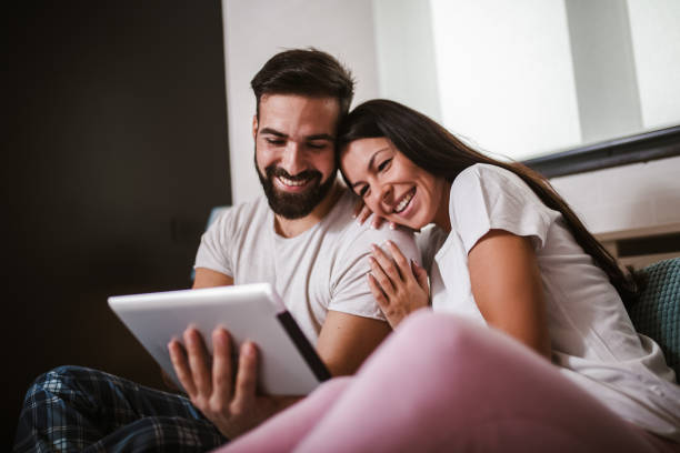 istock Smiling relaxed young couple using digital tablet in bed at home 1288982955