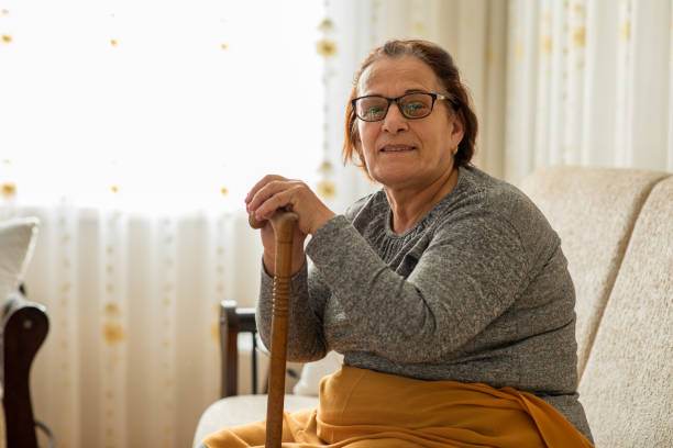 donna anziana seduta a casa con bastone da passeggio - fragility foto e immagini stock