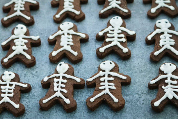 istock Full frame image of rows of homemade, people-shaped, chocolate biscuits on greaseproof parchment baking paper, cookies iced as skeletons with white icing, focus on foreground, Halloween themed party food 1288986430
