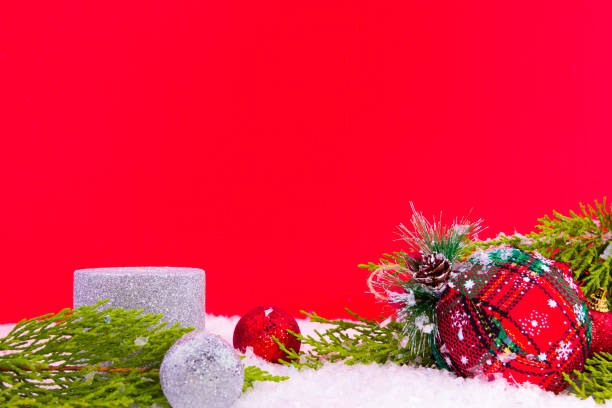 close-up red christmas decorations, snow and pine tree on snowy ground and red wall stock photo