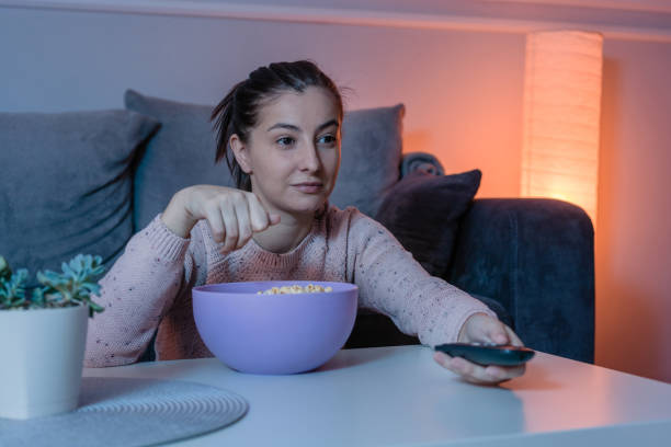 istock Young woman holding remote control at home 1288986489