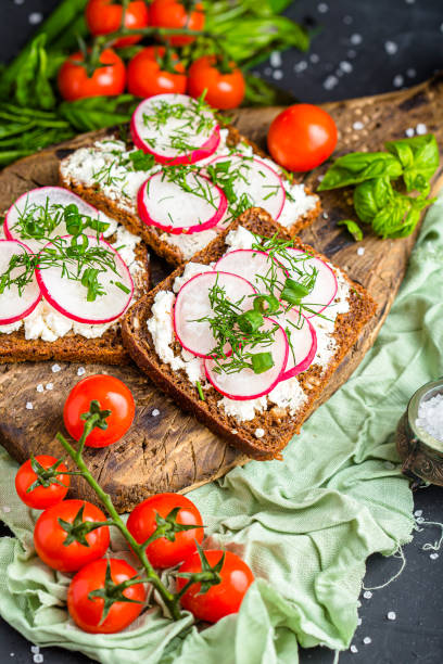 istock cottage cheese on a cracker, several sliced black bread, with radish sliced into wedges with dill, top and side shot, on a wooden cutting board, on a white isolated background 1288988796