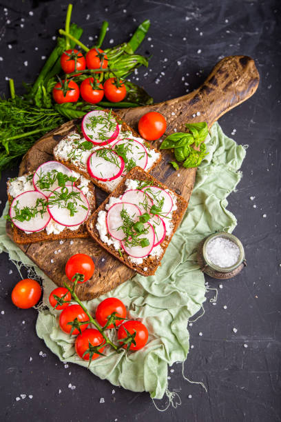 istock cottage cheese on a cracker, several sliced black bread, with radish sliced into wedges with dill, top and side shot, on a wooden cutting board, on a white isolated background 1288988805