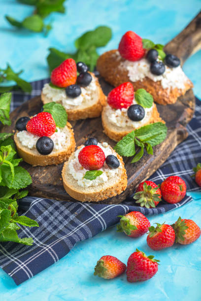 istock cottage cheese on several sliced, round white bread, berries, strawberries and blueberries with mint, top and side shot, on a wooden cutting board, on a light blue isolated background 1288988808