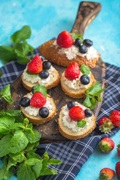 istock cottage cheese on several sliced, round white bread, berries, strawberries and blueberries with mint, top and side shot, on a wooden cutting board, on a light blue isolated background 1288988821