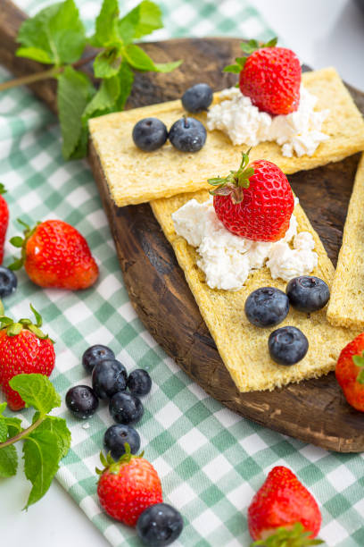 istock cottage cheese on several crackers, crisps with berries, strawberries and blueberries with mint, top and side shot, on a wooden cutting board, on a white isolated background 1288989917