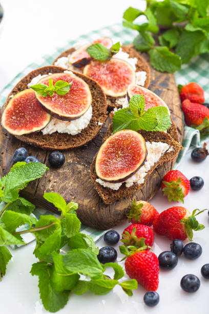 istock cottage cheese on a cracker, several sliced black bread, with sliced figs with mint, top and side shot, on a wooden cutting board, on a white isolated background 1288989941