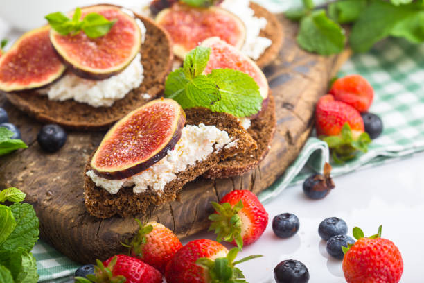 istock cottage cheese on a cracker, several sliced black bread, with sliced figs with mint, top and side shot, on a wooden cutting board, on a white isolated background 1288989963